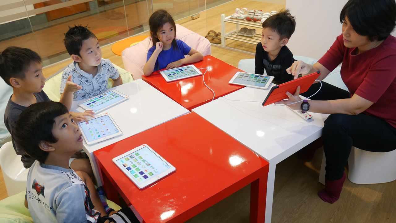 Young children at a bright table using tablets with an LCCL teacher in the Early Creators class