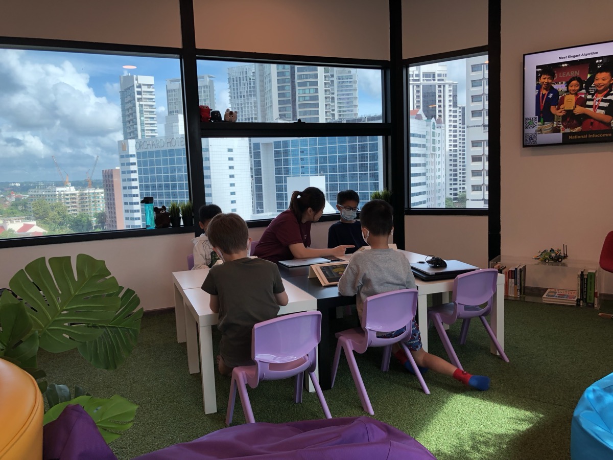 LCCL coding classroom on Orchard Road, Singapore — children at laptops with the city skyline behind them